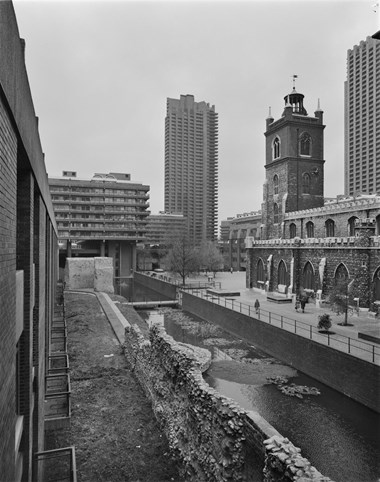 A black and white photo of the Church of St Giles next to a narrow lake, showing Lauderdale Tower in the Background.