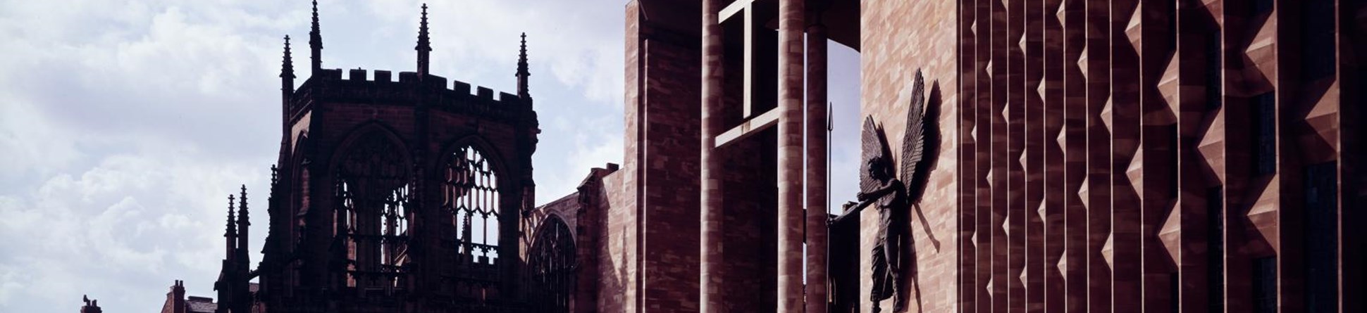 Colour photo of the porch of Coventry Cathedral with the ruins of the old cathedral behind and to the left.