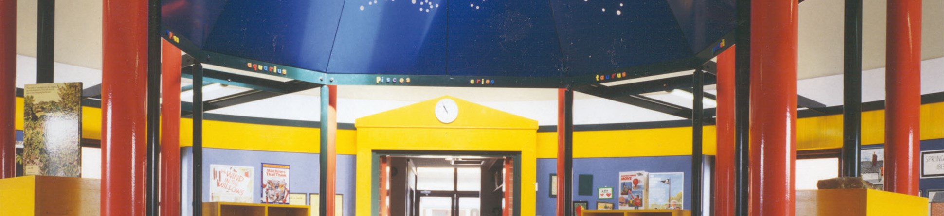 The interior of the Bishop Wilson Memorial Library shows the bright red columns, blue painted canopy and yellow door frames, shelves and wall coverings.