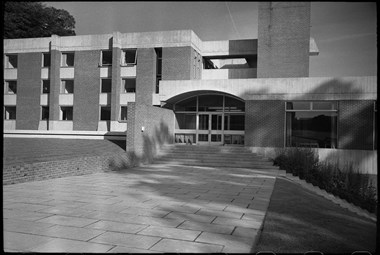 The front entrance has a concrete band with elliptical arch over the porch. Behind the block has alternating bands of concrete and windows.