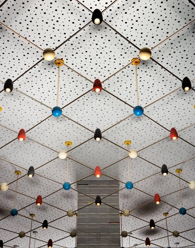 white lights with multi coloured lampshades suspended from a ceiling. The ceiling is white with dark speckles and square patterns