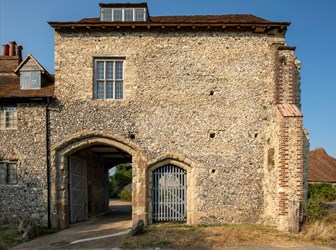 Stone two-storey building with large arched gateway running through the building at ground level on the left.