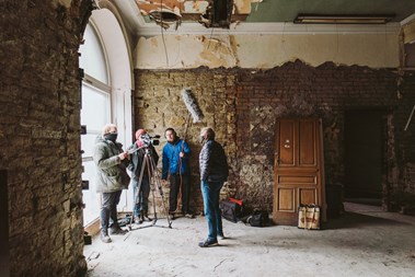 Film crew of three film one subject in a room that's undergoing renovation work.