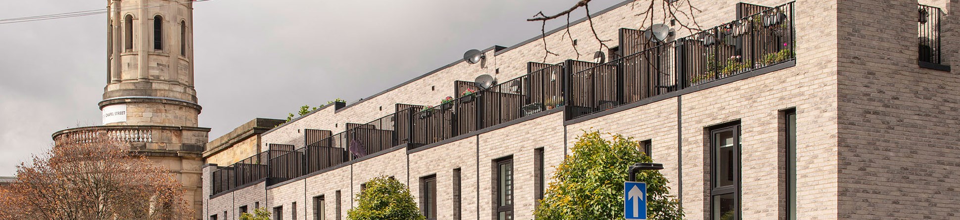 A view of a terrace of modern brick housing adjacent to a neoclassical church with a clock tower.