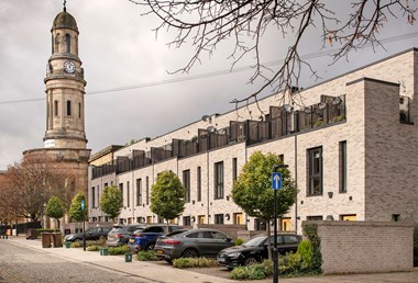 A view of a terrace of modern brick housing adjacent to a neoclassical church with a clock tower.