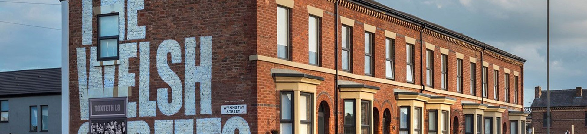 Refurbished Victorian brick terraced housing,  'The Welsh Streets' is painted in large lettering on the near gable end.