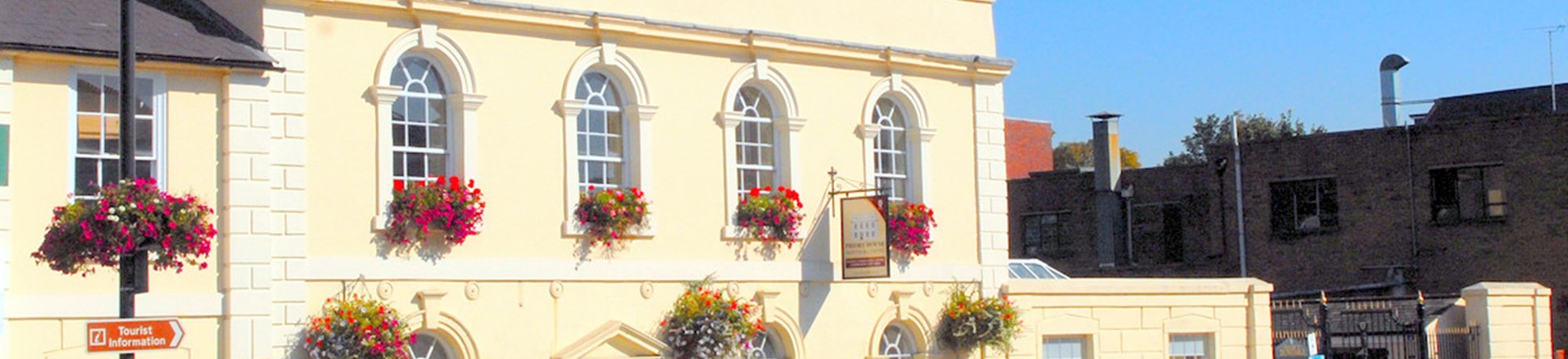 The image shows the exterior of Priory House with a butter yellow exterior paint and white around the window frames.