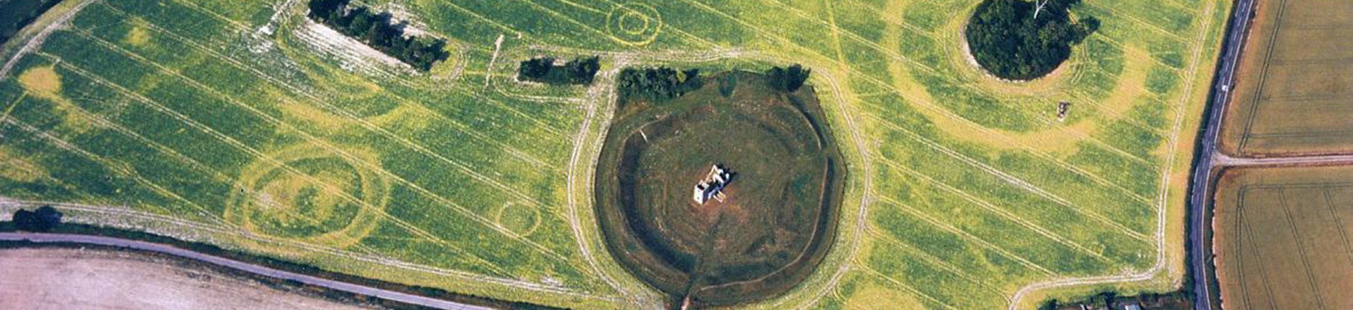 Colour aerial photograph of fields in crop with a ruined church sitting within an earthwork bank