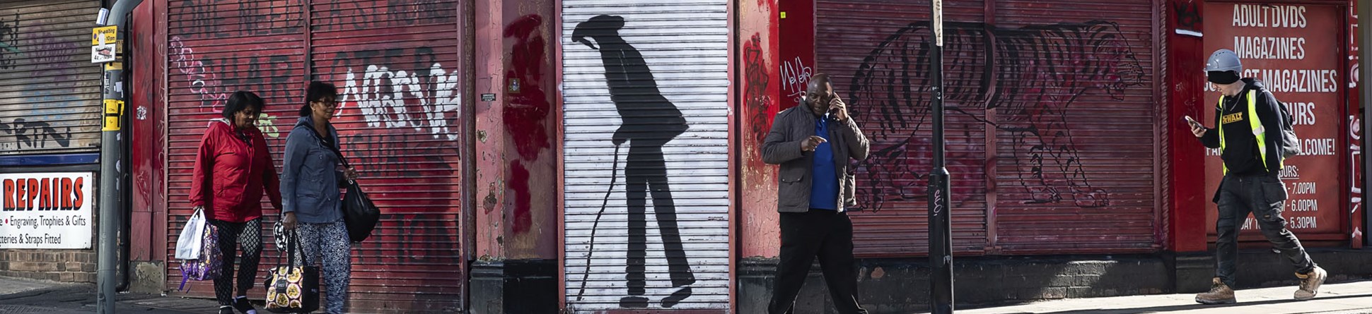 Pedestrians passing a shuttered shop on a street corner.