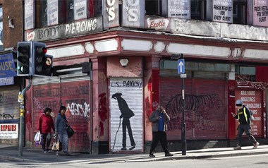 Pedestrians passing a shuttered shop on a street corner.