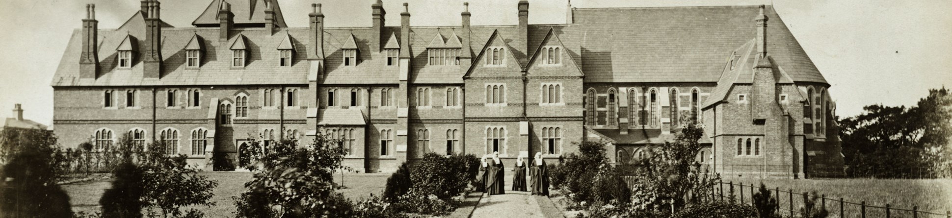 Looking along a gravel path towards the south range of the St Peter's Convent, with four nuns standing in the distance. 