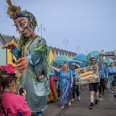 A street carnival puppet followed by a procession of people in Lowestoft.