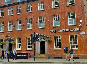 Pedestrians pass in front of a broad-fronted 3-storey red-brick town building with signs saying "The Waterhouse", "Free House" and "Princess Street".