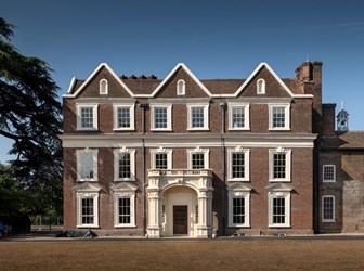 Front view of Boston Manor House, a red brick building with 3 storeys, white windows and a decorative porch.