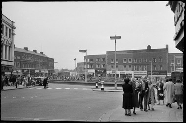 archive black and white photograph of a busy street scene with people on the pavements