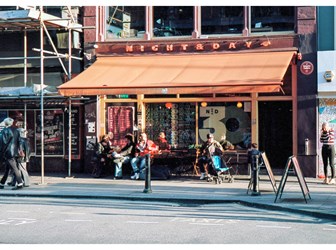 A view from across the street of the Night and Day Café, with people sitting at tables outside