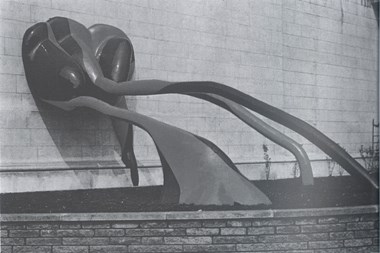 Sculpture in flower bed leaning up against a wall