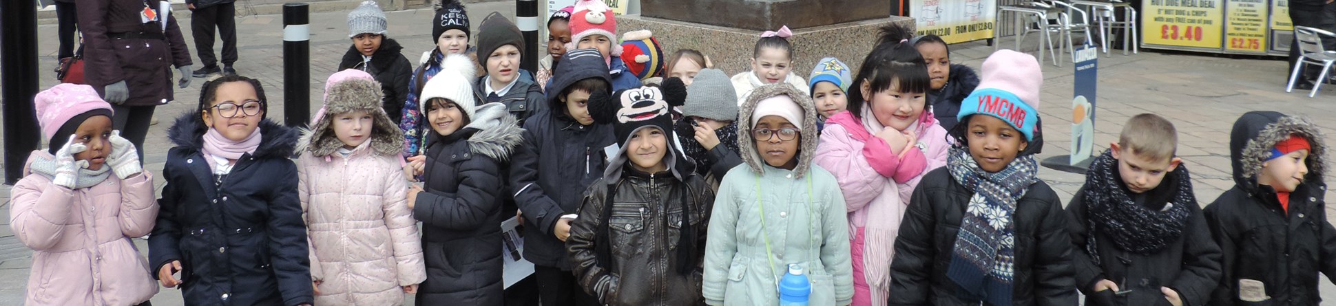 A group of about 20 Year 1 children posing for a group photo in front of Alice Hawkins statue in Leicester.