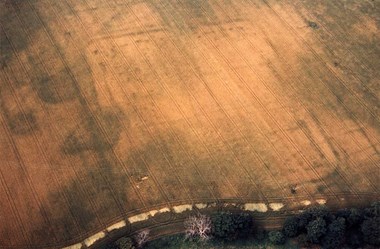 Colour aerial photo showing an arable field with the archaeology seen faintly as darker lines against a paler background.