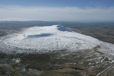 Colour aerial photo showing a flat topped hill rising from an upland moorland landscape with dry stone walls and streams