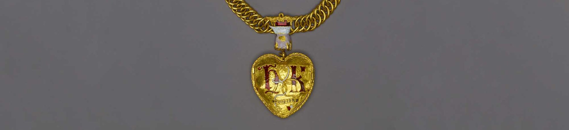 A large, heart-shaped gold pendant on a thick gold chain, suspended from a hand-shaped ornamentation, and detailed with a rose and pomegranate. 