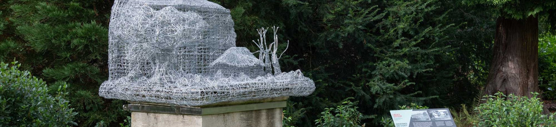 An installation comprising a wire sculpture of plantation structures, set on an existing stone plinth in a country house garden.