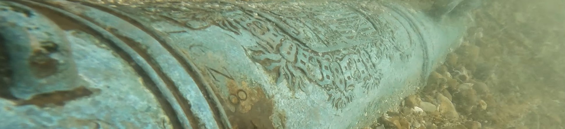 Iron cannon lying on shingle under water