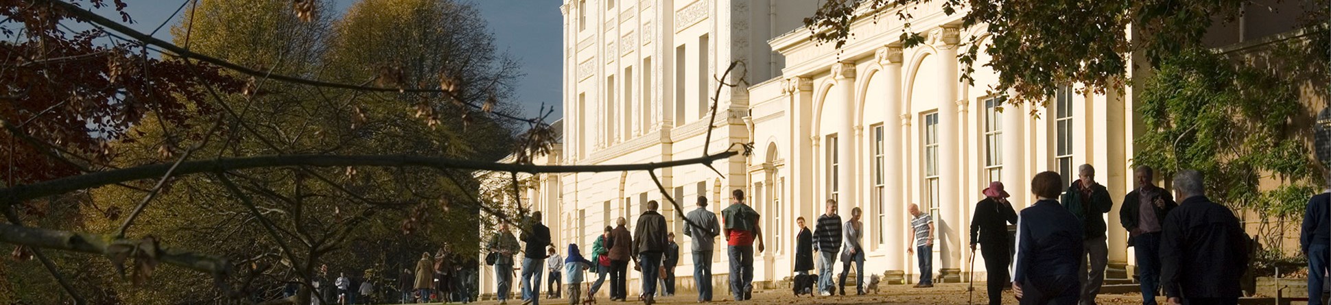 Photo of the a sunlit front of Kenwood House with people walking along the path in front