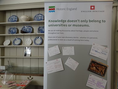 A vertical banner bearing the message "Knowledge doesn't belong to universities or museums" The banner invites participants to share their discovery stories, examples are written on cards pinned to the banner.