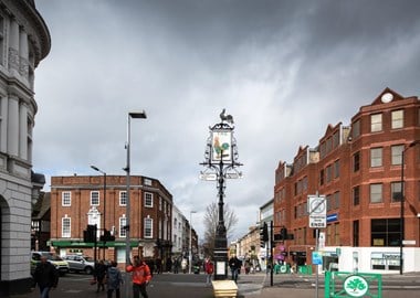 Busy high street junction with an old sign of the former Cock Tavern Public House in the centre.