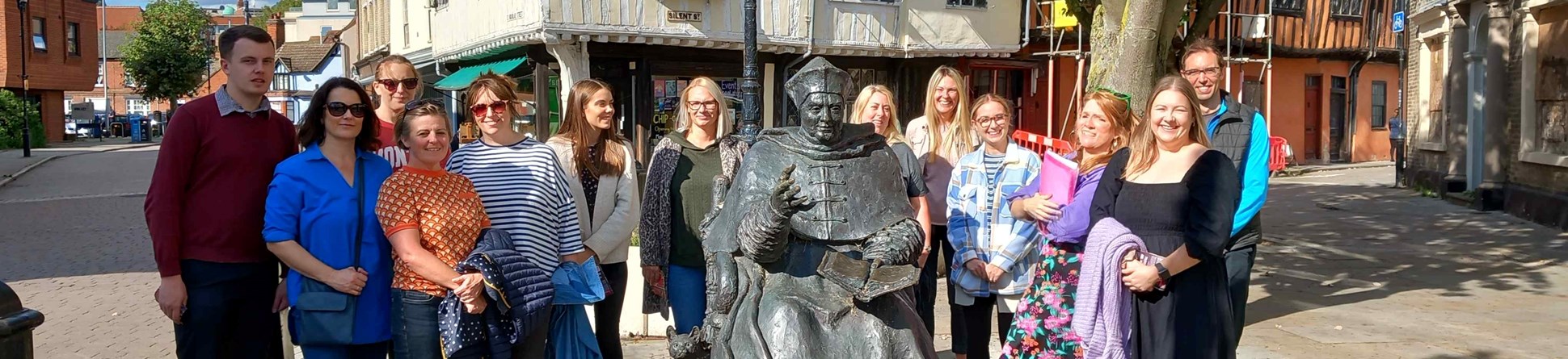 A group of teachers stand around a statue of Thomas Wolsey in Ipswich town centre.