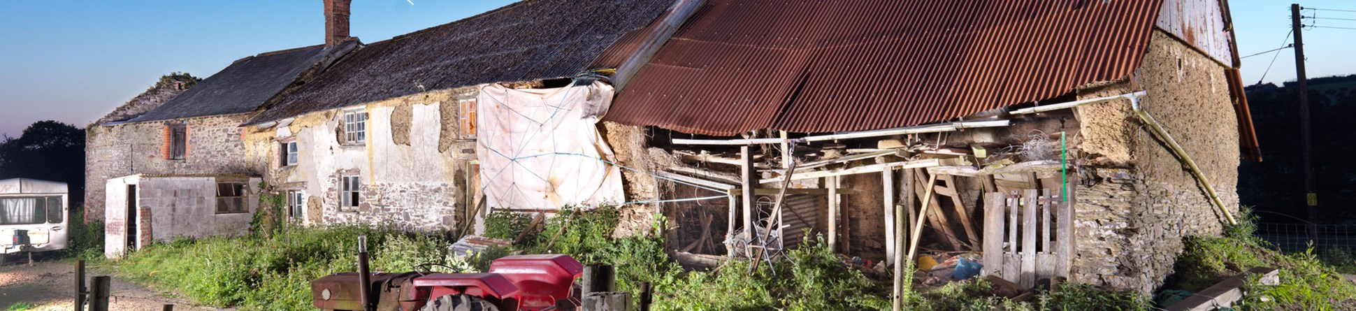 A farmhouse flanked by derelict outbuildings.