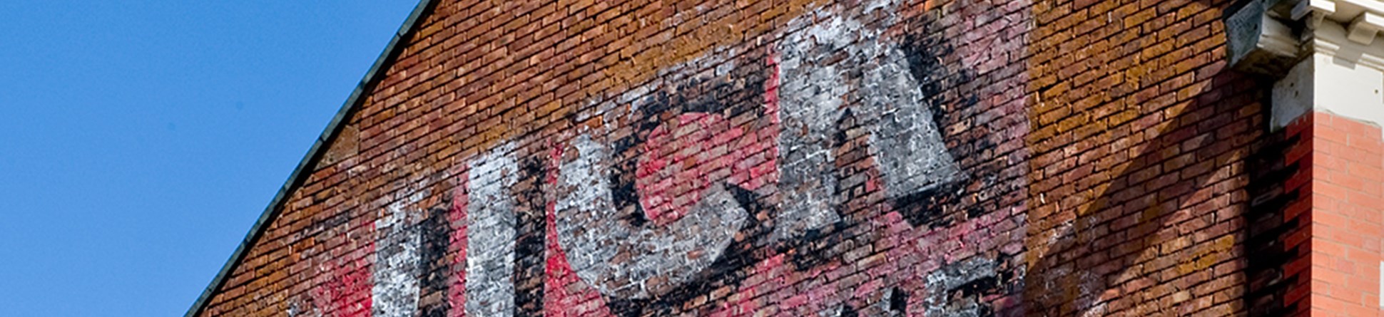 Image of the side of a brick building with a red faded advertising sign for matches.