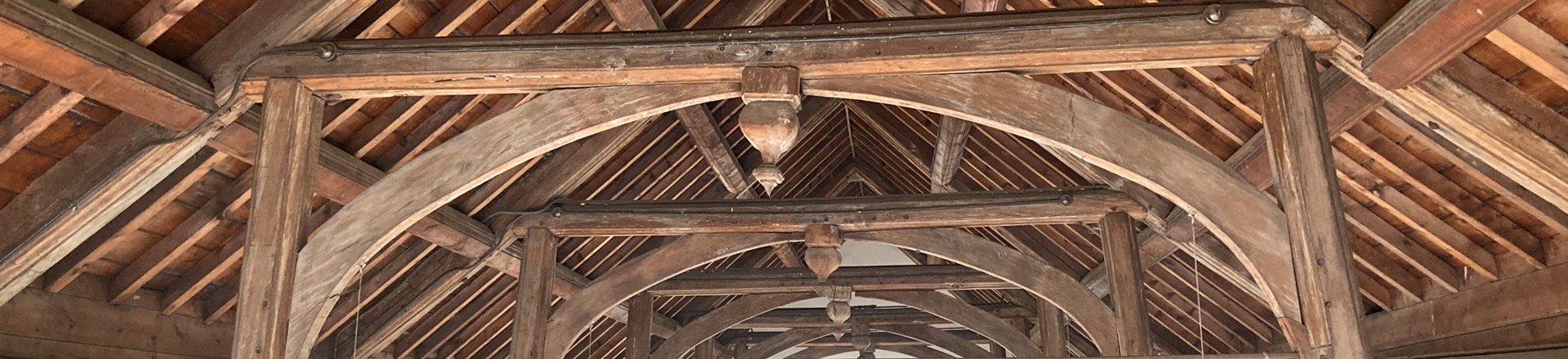 The wooden hammerbeam roof of Becket's Chapel can be seen. Wooden timbers with a series of central wooden arches. The arched plain glass chapel window can be seen in the background.