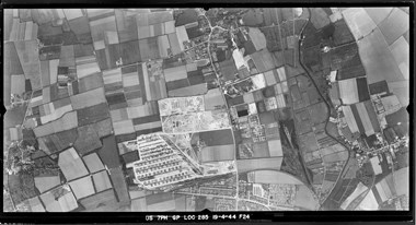 A black and white vertical aerial photograph showing a storage depot and camp bounded by roads and a patchwork of fields.
