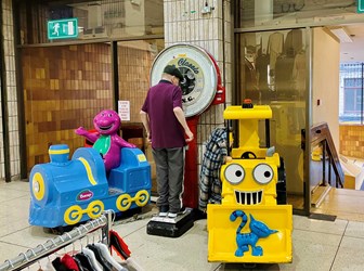 Interior view of Kirkgate Market, showing a man weighing himself, and two children's rides.