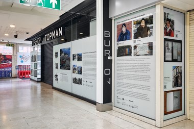 Exhibition display on internal shopping centre windows at a now empty shop unit with the Topman logo above.