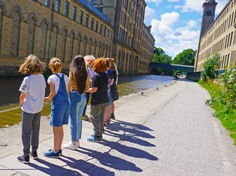 A group of children and one adult hold a rope on a canal towpath in an industrial landscape.