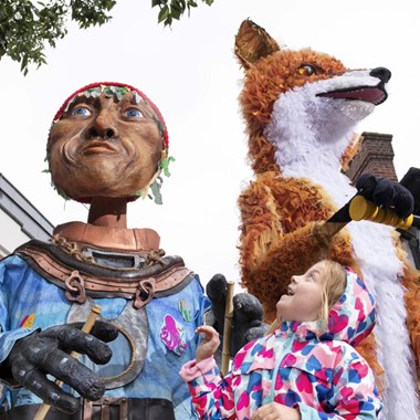 A young girl looking up in surprise at two large street puppets above her.