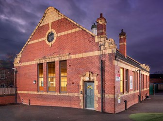 Exterior view of a red-brick school building lit at twilight under dark purple skies