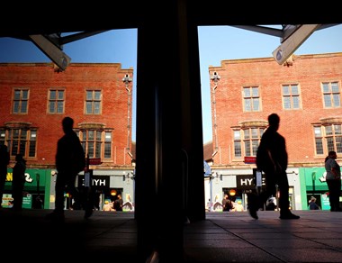 Silhouettes of people walking along a high street.