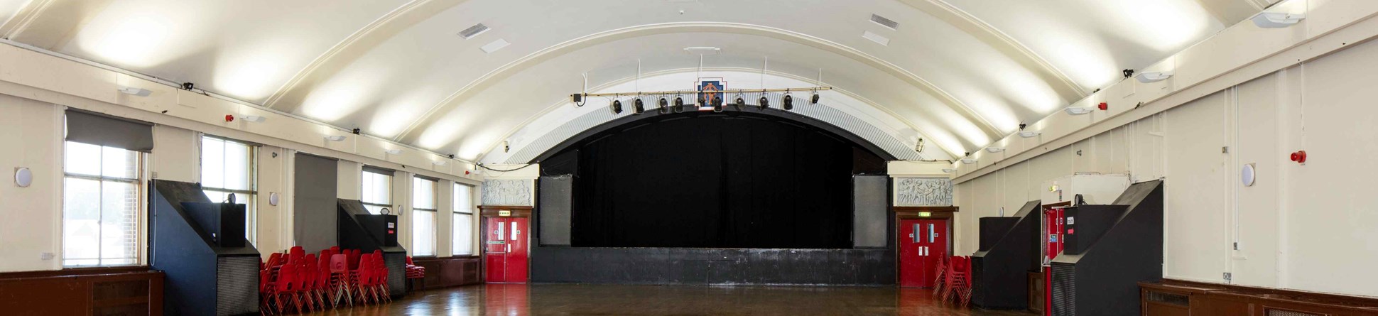 View up the length of a large ballroom with highly-polished wooden floor, white walls and slightly domed ceiling.