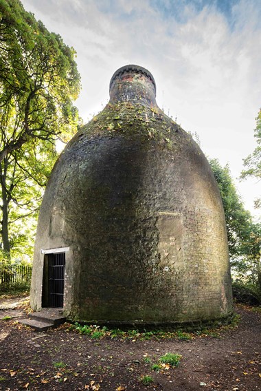 A brick bottle-shaped structure situated in a wooded area.  