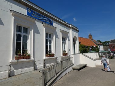 Single storey white building with three large windows and an arched door at the far end.